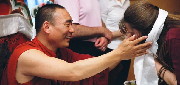 Khentrul Lodrö T’hayé Rinpoche with many people in the background, smiling and extending his hands towards a bowing woman.